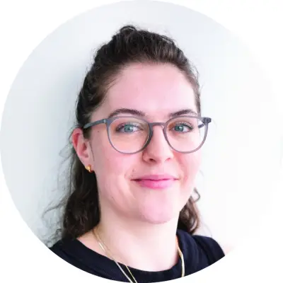 Sophie Molloy is a young woman with brown curly hair. She is looking to the right, has a small smile on her face and is wearing large rounded glasses..