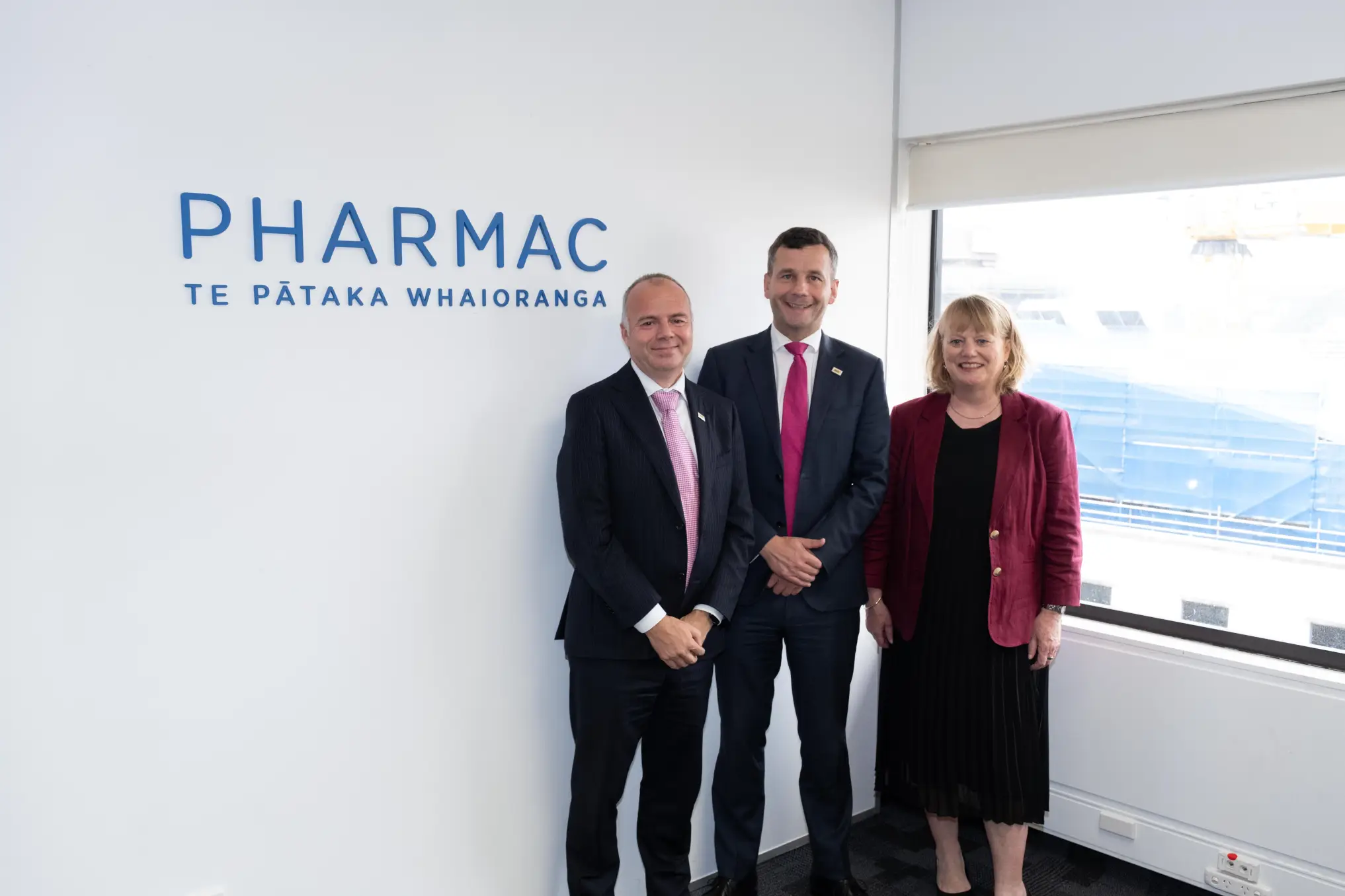 Todd, David and Sarah stand next to the Pharmac logo. .