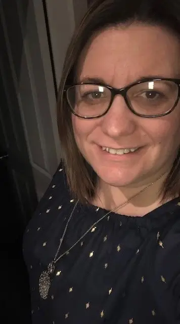 Lisa smiles at the camera. She is leaning on a wall with a doorway in the background..